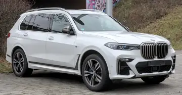 Białe BMW x7 z przyciemnianymi szybami i chromowanymi felgami stoi na brukowanym podjeździe.