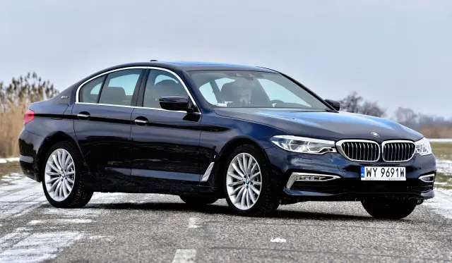 Ciemnogranatowe BMW 530e z napisem "eDrive" na błotniku, zaparkowane na drodze z resztkami śniegu.