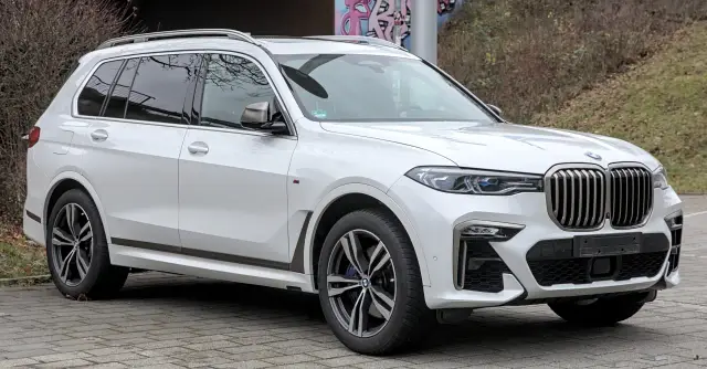 Białe BMW x7 z przyciemnianymi szybami i chromowanymi felgami stoi na brukowanym podjeździe.