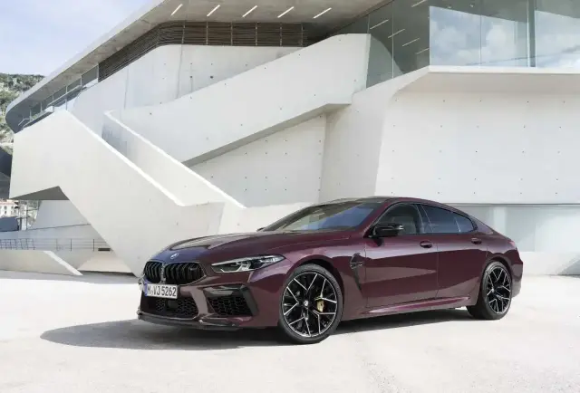 Eleganckie, ciemnoczerwone BMW M8 Gran Coupe prezentuje się na tle nowoczesnej architektury.